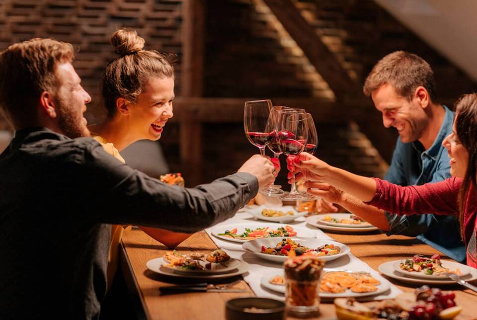 grupo de pessoas brindando com sorriso no rosto em uma mesa de jantar