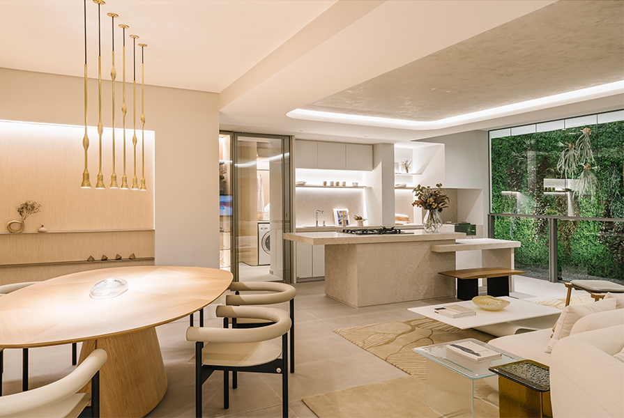 Um ambiente integrado com sala de jantar e cozinha com uma mesa de jantar oval de madeira, cadeiras estofadas e uma ilha de cozinha com bancada. 